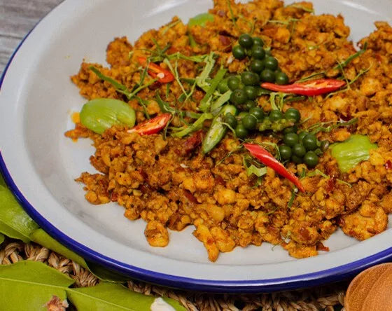 Thai basil stir fry with minced meat, red chillies, fresh peppercorns, and aromatic herbs served on a white plate.